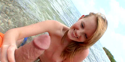 A smiling blue eyed honey is playing with a dick on the beach