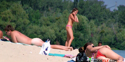 Nude beach girl sunbathes next to her man outdoors