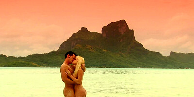 A blonde is by the ocean with her lover and she is kissing him there