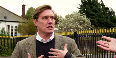 A brunette with glasses is licking a cock next to some tiles