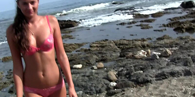 A brunette is naked at the beach, masturbating and sucking dick