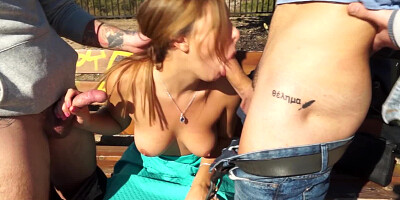 Hot brunette is sucking two dicks in a threesome on the bench
