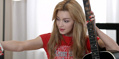 An anal loving redhead is on the bed, playing with a guitar